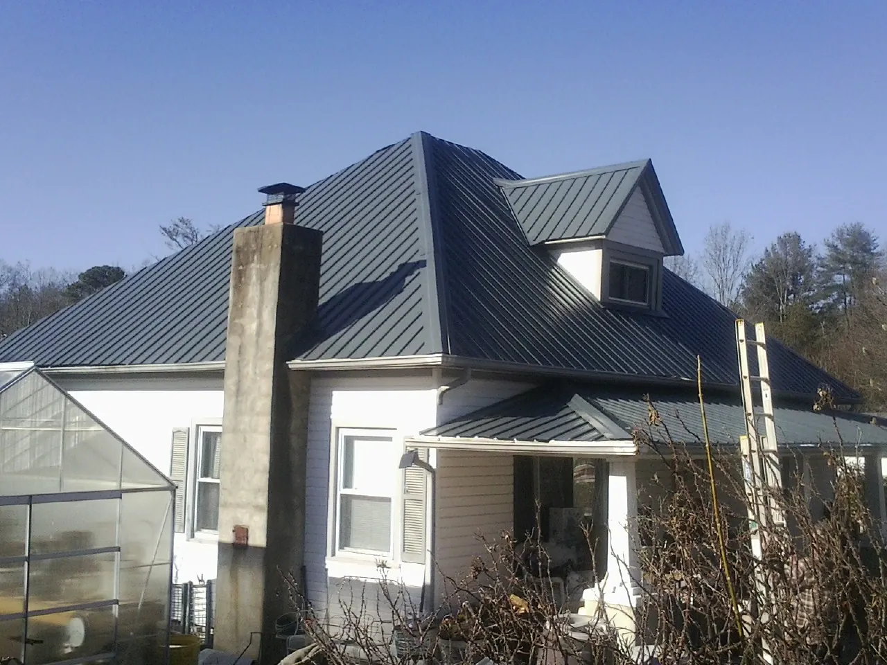 Dark blue standing seam metal roof on a white farmhouse with dormer in Eldora