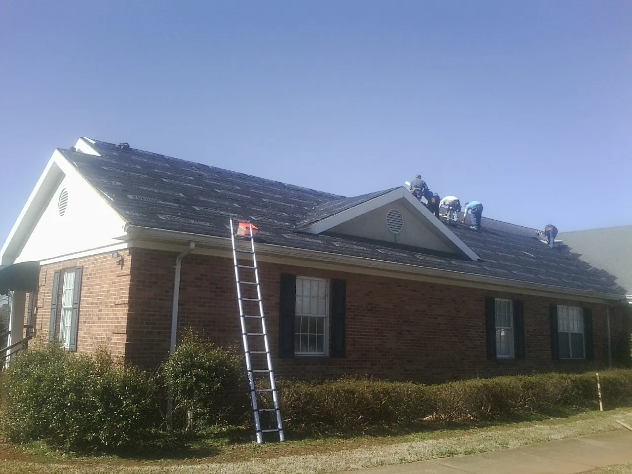 Crew tearing shingles off a brick ranch roof with a ladder set — Emergency Roof Repair work by our crew in Eldora