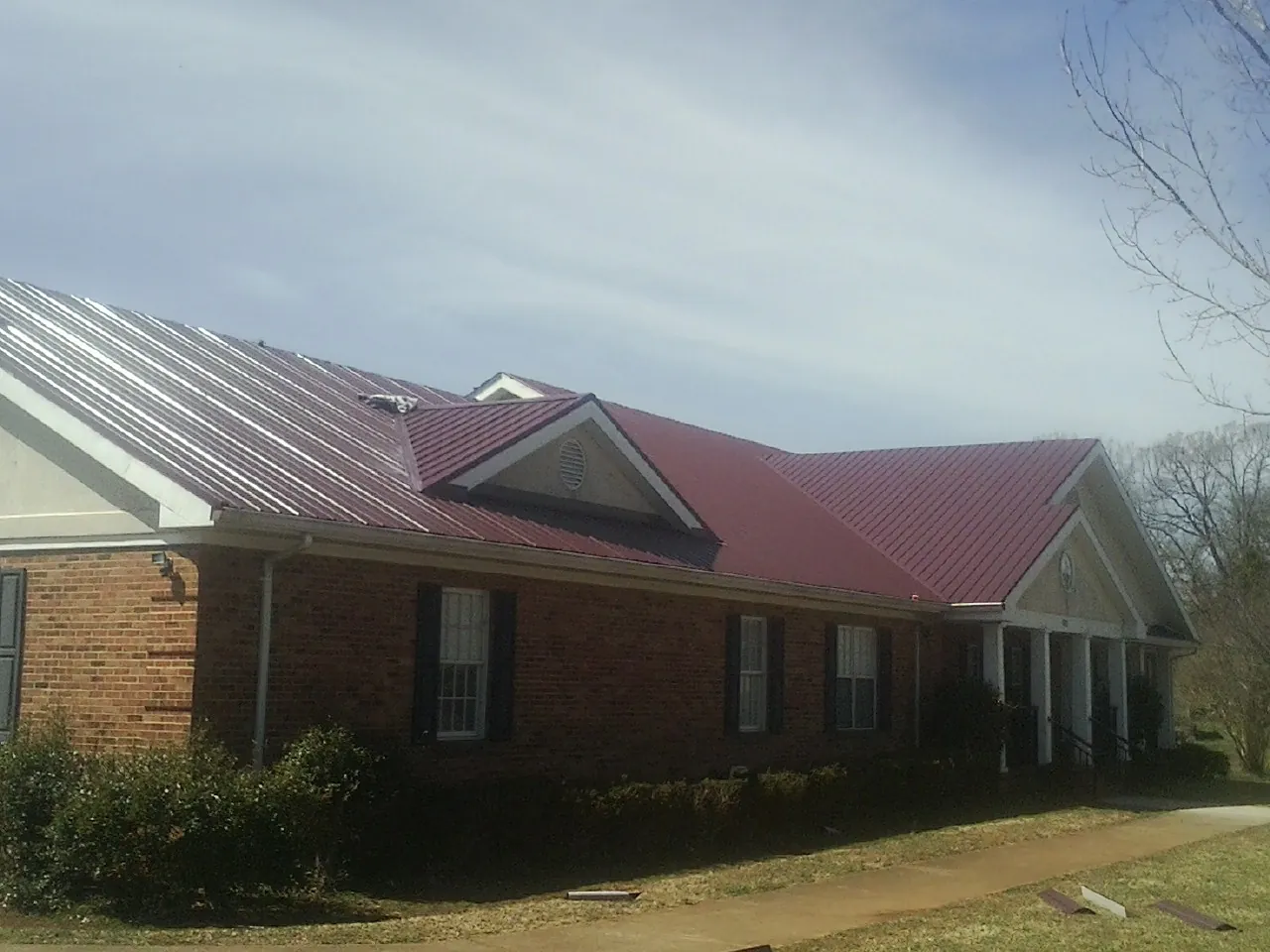 Red metal roof with gabled entries on a long brick building, from a Hail Damage Roof Repair job in Eldora