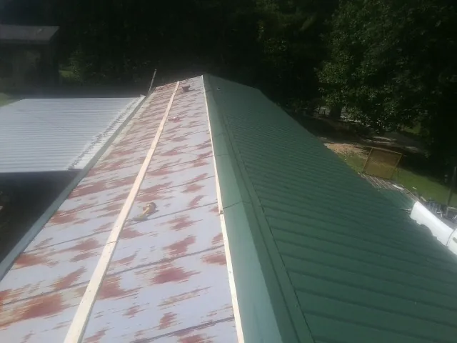 Old rusted panels beside newly installed green metal roofing — Wind Damage Roof Repair by Roofing Brothers in Eldora