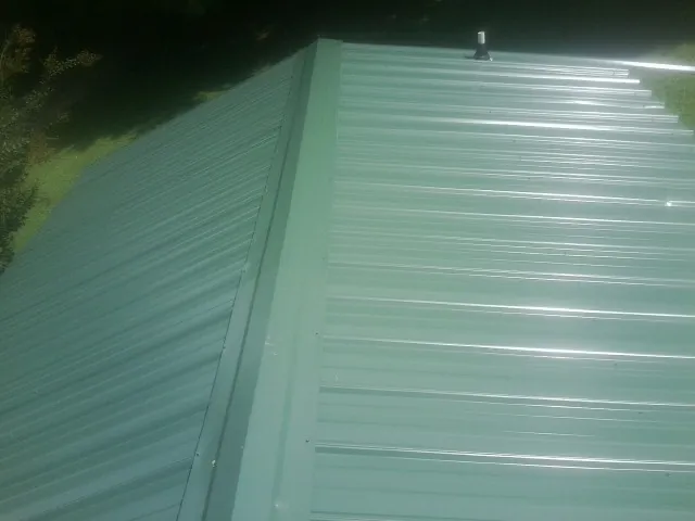 New green metal panels meeting at the ridge of a roof — Flat Roof Repair work by our crew in Eldora