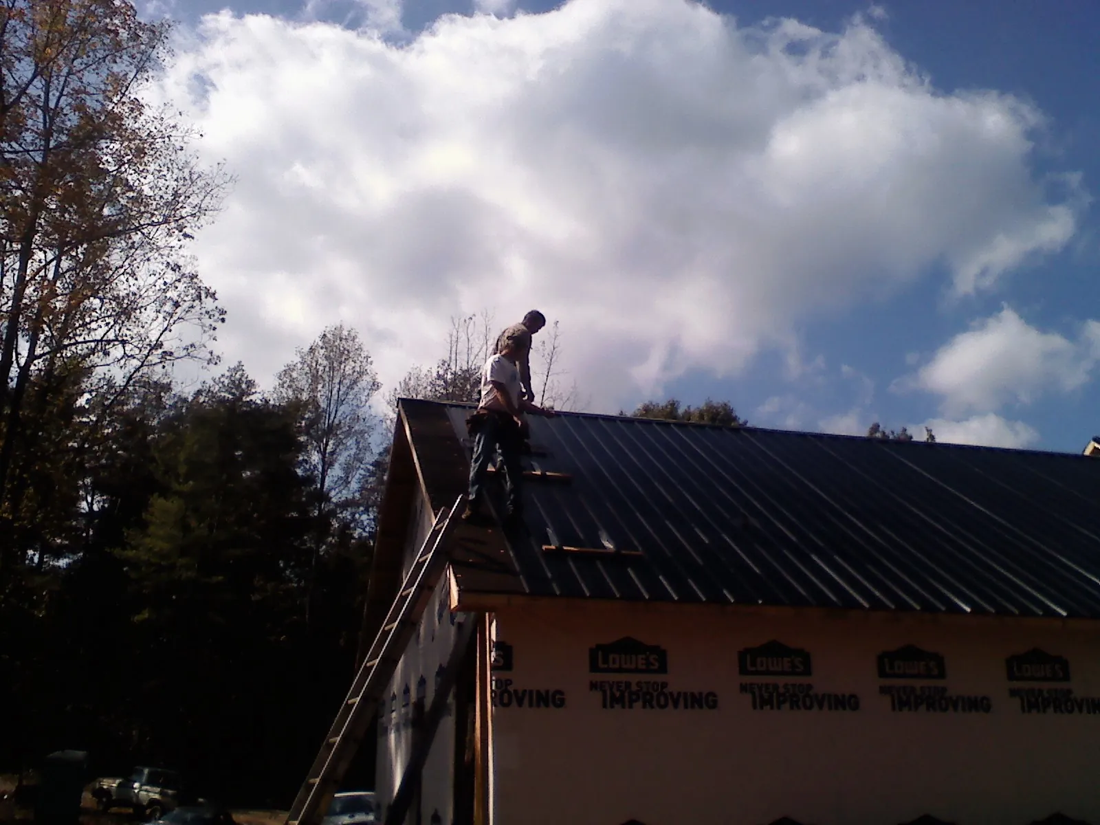 Roofer fastening dark metal panels high against a cloudy sky, from a Roof Inspection job in Eldora