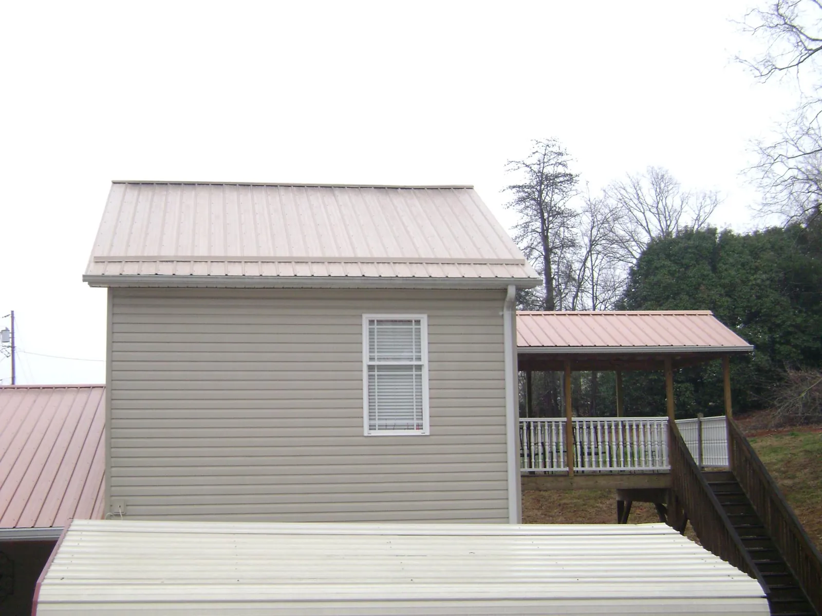 Tan metal roofs on a two story addition and attached porch, from a Roof Replacement job in Eldora
